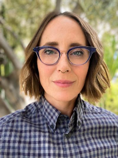 Close-up portrait of a person wearing purple glasses and a blue-and-white checkered shirt outdoors.